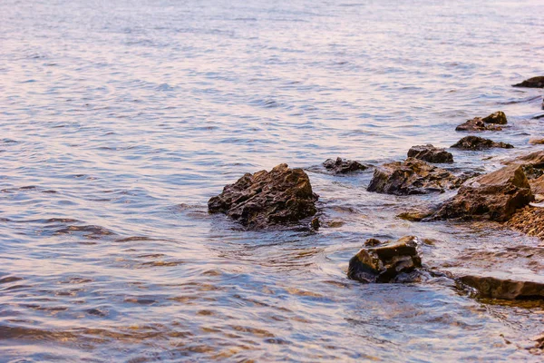 Piedra cerca del río. Las olas corren en la costa. Puesta de sol de verano. Los rayos del sol se reflejan en el agua —  Fotos de Stock