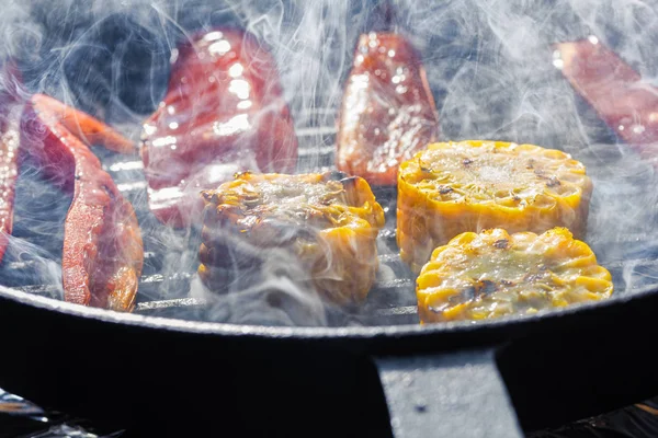 Smoke and steam rise above the vegetables in a grill pan