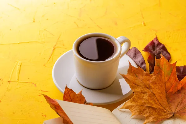 Concepto de otoño. Una taza de espresso, un bloc de notas en blanco y follaje de caída sobre una mesa de hormigón amarillo. Copiar espacio —  Fotos de Stock