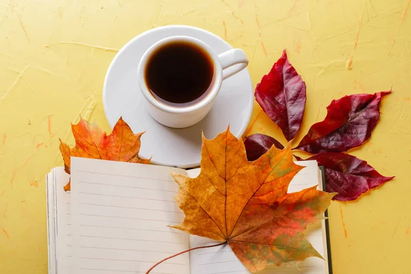 Concepto de otoño. Una taza de espresso, un bloc de notas en blanco y follaje de caída sobre una mesa de hormigón amarillo. Acostado. Copiar espacio —  Fotos de Stock