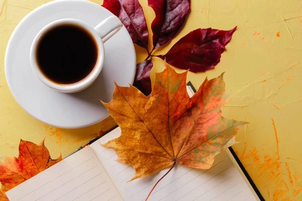 Café de otoño. Una taza de espresso, un bloc de notas en blanco y follaje de caída sobre una mesa de hormigón amarillo. Acostado. Primer plano —  Fotos de Stock