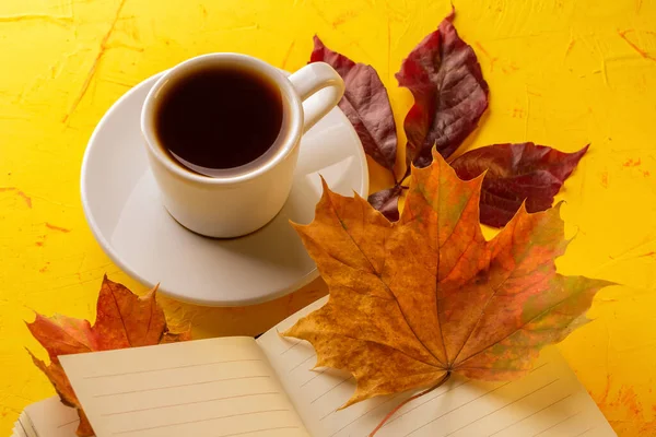 Concepto de otoño. Una taza de espresso, un bloc de notas en blanco y follaje de caída sobre una mesa de hormigón amarillo. Primer plano —  Fotos de Stock