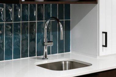 Beyaz mermer bir tezgahta parlak mavi kaplama döşeme, cilalı krom musluk ve kahverengi ve beyaz dolaplar içeren bir mutfak musluğu detayı..