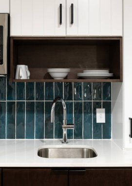 Beyaz mermer bir tezgahta parlak mavi kaplama döşeme, cilalı krom musluk ve kahverengi ve beyaz dolaplar içeren bir mutfak musluğu detayı..