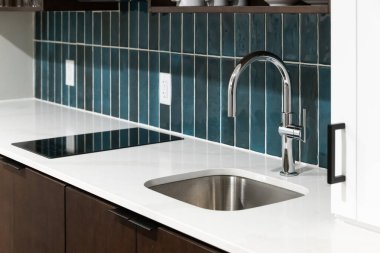 Beyaz mermer bir tezgahta parlak mavi kaplama döşeme, cilalı krom musluk ve kahverengi ve beyaz dolaplar içeren bir mutfak musluğu detayı..