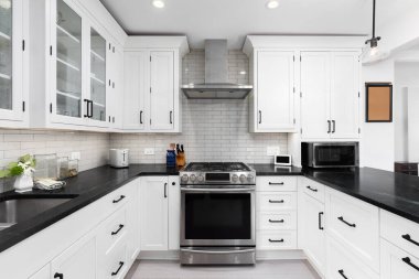 Beyaz dolapları, metro fayansları, paslanmaz çelik aletleri, siyah tezgahları ve donanımları olan bir mutfak detayı..