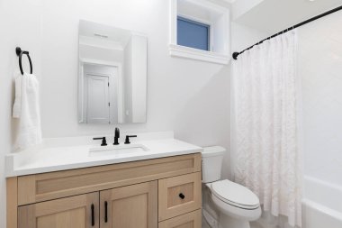 Beyaz meşe kabini olan bir banyo, beyaz mermer tezgahta siyah musluk, ve beyaz ringa kemiği duşu..