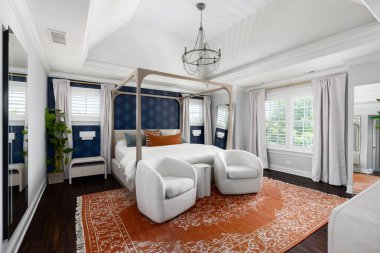 A cozy bedroom with chandelier hanging from a coffered ceiling, a blue wallpaper accent wall, and a canopy bed on an area rug and dark hardwood floor. No brands or labels.