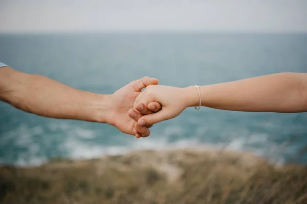 Mans hand and womans hand keeping each other, seashore on the background. The touch of a hands.