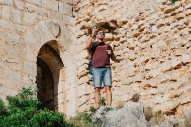 Dağlarda kalan ve Dağları cep telefonu üzerinde antik kale yakınında sunset Bulvarında İspanya'yakalama sırt çantası olan bir adam. Gezgin dağlarda.