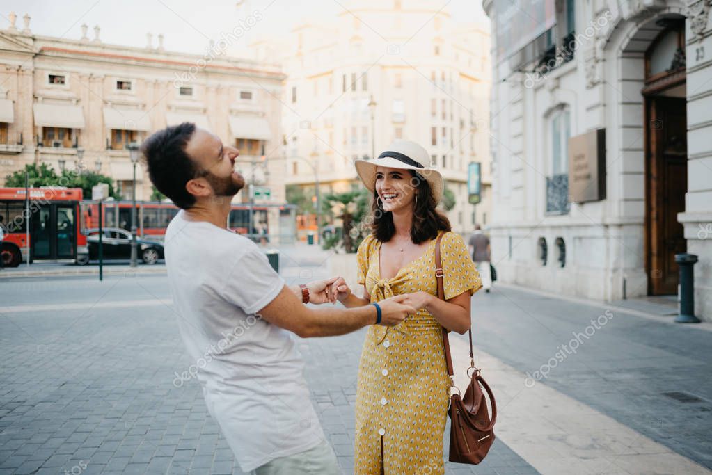 Awesome brunette girl in the hat with her boyfriend with beard trying to dance together on the old European street in Spain on the sunset