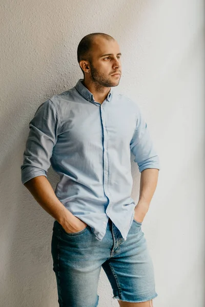 Tutuşup ceplerinde İspanya penceresinde yakınındaki beyaz duvarlı dairede poz mavi gömlek ve mavi kot şort tabaklanmış acımasız adam