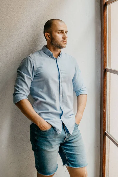 Düşünme tutuşup ceplerinde İspanya penceresinde yakınındaki beyaz duvarlı dairede tabaklanmış acımasız adam mavi tişört ve kot şort