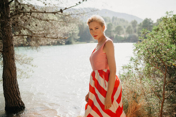 An attractive blonde woman in the red and white dress near the mountain lake. Spain