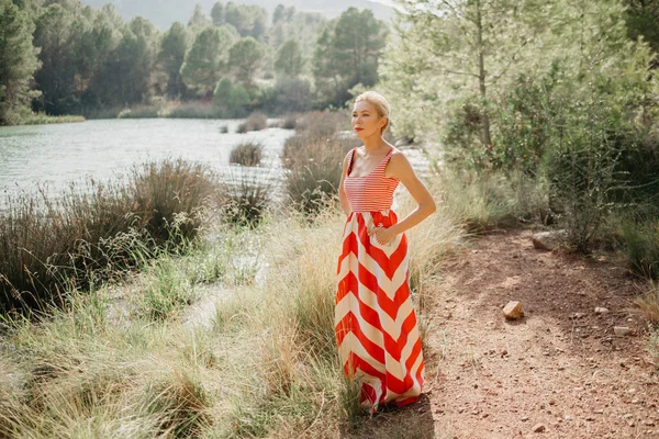 山の湖の沼に近いポーズ赤と白のドレスでスタイリッシュなかなりブロンドの女性 スペイン — ストック写真