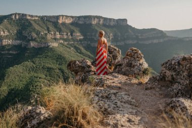 Bir şık genç sarışın Bayan Kanyon taşlar arasındaki uçurumun üstünde poz kırmızı ve beyaz elbiseli. Portre arkadan. İspanya