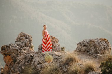 Taşlar arasında uçurumdaki poz kırmızı ve beyaz elbiseli bir şirin sarışın kadın. İspanya