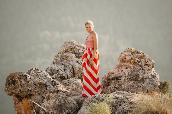 背景の山の崖の上に踊る赤と白のドレスでかわいい金髪女性 マウンテン ビュー スペインの夜 — ストック写真