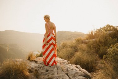 Çekici bir genç sarışın kadın onu geri Antik Kanyon ile turuncu günbatımı üzerinde poz kırmızı elbiseli. İspanya