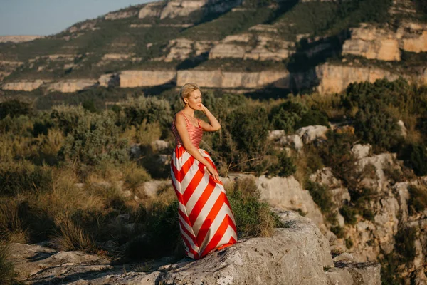 夕暮れの古代峡谷でポーズをとって赤いドレスでスタイリッシュなブロンドの女の子 スペイン — ストック写真