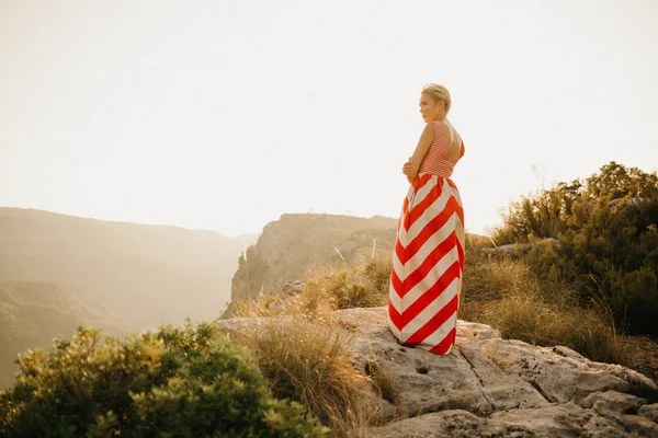オレンジ色の夕日に古代峡谷の背中でポーズ赤いドレスで腕をかなりブロンドの女の子を渡った スペイン — ストック写真