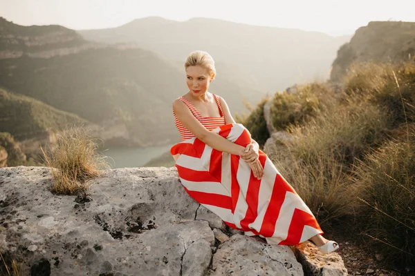 オレンジ色の夕日古代峡谷の大きな石に座っている優雅な金髪の若い女性スペイン — ストック写真