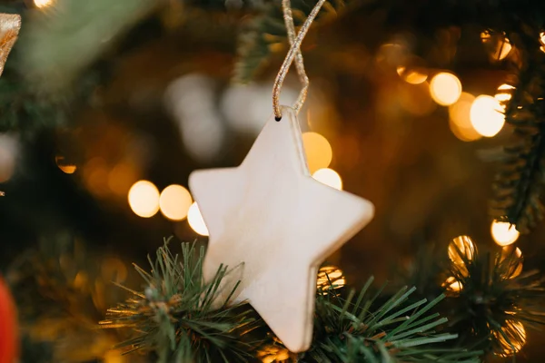 Close photo of a single wooden star on a green Christmas tree with a warm yellow garland.