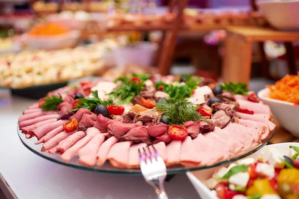 Different types of meat slices with herbs, dried tomatoes and olives lying radially on a round plate in the restaurant.