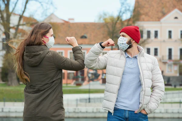 Elbow bumping. Elbow greeting to avoid the spread of coronavirus (COVID-19). A man with a beard and a woman with long hair in medical masks bump elbows instead of greeting with a hug or handshake.