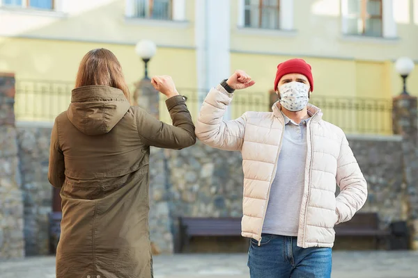 Elbow bumping. Elbow greeting to avoid the spread of coronavirus (COVID-19). A woman and a man in medical face masks bump elbows instead of greeting with a hug or handshake in the old town.