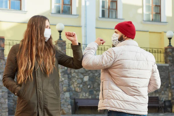 Elbow bumping. Elbow greeting to avoid the spread of coronavirus (COVID-19). A man and a woman in medical face masks bump elbows instead of greeting with a hug or handshake in an old street.