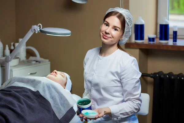 Attraktiv Kvindelig Kosmetolog Smilende Udgør Med Hudpleje Gel Nær Patient - Stock-foto