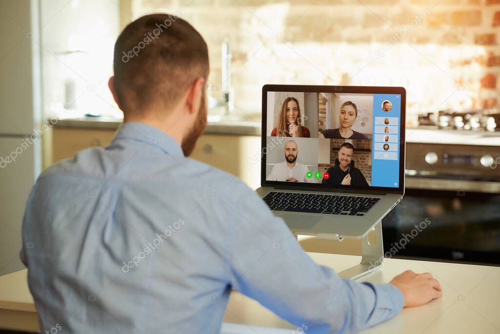 Back view of a male employee who works remotely listening to his colleagues about business in a video call on a laptop computer at home. A multiethnic business team at an online meeting.
