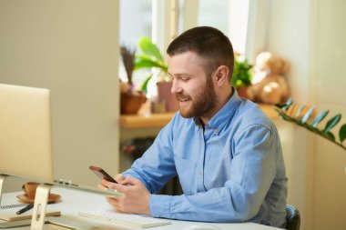 Mavi tişörtlü mutlu genç bir patron evinde dizüstü bilgisayarın önünde akıllı telefondan haber arıyor. Evden uzakta çalışan sakallı bir adam.. 