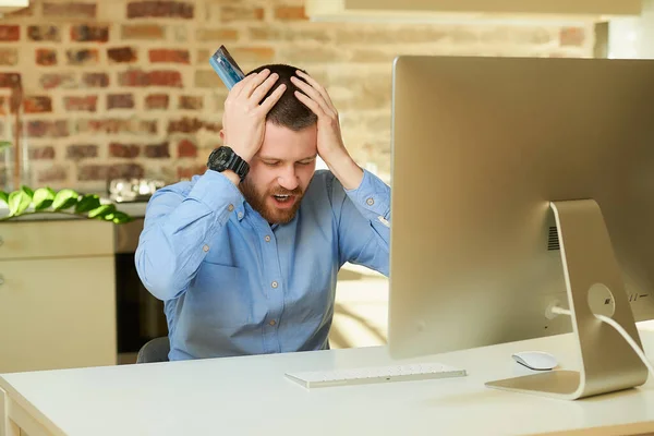 A man upset by the prices on an online store and putting hands with a card on his head in front of the computer. A guy doing an online payment on the internet on a desktop computer in his apartment.