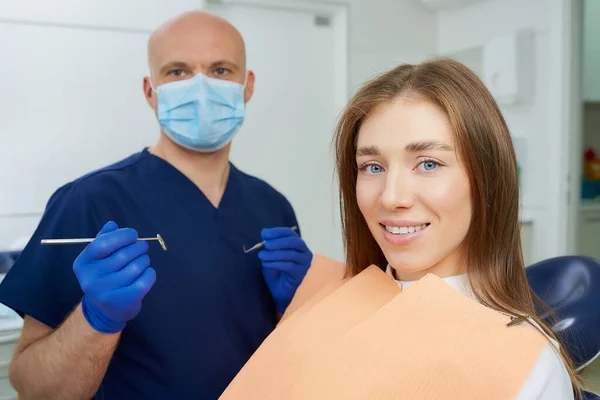 Dentysta Masce Medycznej Trzyma Lusterko Dentystyczne Stomatologa Pobliżu Uśmiechniętej Pacjentki — Zdjęcie stockowe