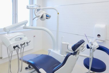 Beyaz ve mavi mobilyalı, dişçi sandalyeli, matkaplı modern bir dişçi ofisi. Dişçinin ofisi..