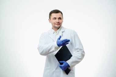Beyaz laboratuvar önlüklü ve mavi tek kullanımlık eldivenli kibar bir erkek doktor bir elinde karton, diğer elinde de işaret ediyor. Bir bilim adamı beyaz arka planda izole edilmiştir..