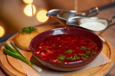 Ukrayna borsch 'unun yakın bir fotoğrafı pampuşka, yeşil soğan ve ekşi krema ile birlikte bir restoranın masasındaki ahşap tepside..