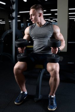 Spor salonunda kaslı bir adam dizlerinin üzerinde dambıllar tutuyor. Vücut geliştirici, vücut geliştirme yarışmasına hazırlanmak için dambıllarla egzersiz yapıyor. Bir adam rekabet öncesi diyette..