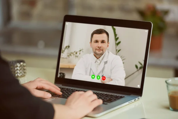 Bir kadının omzunda dizüstü bilgisayar görüntüsü. İnternetteki doktor randevusunda bir kadın. Bir kız beyaz laboratuvar önlüklü bir terapistle videoda sağlığını tartışıyor..