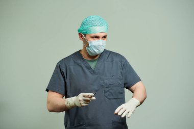 Önlüklü bir cerrah ameliyat odasında bir hastayı kesmek için neşter hazırlıyor. Bir doktor V yaka ameliyat gömleği, tek kullanımlık tıbbi eldiven, tıbbi maske ve şapka giyer..