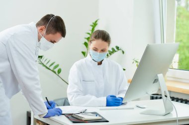 Tıbbi maskeli bir cerrah ve radyoloji uzmanı hastanede bir hastanın analizini tartışıyor. Masaüstü bilgisayarının önünde oturan bir kadın doktor. Yanında bir terapist oturuyor..