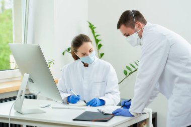 Tıbbi maskeli bir cerrah ve radyoloji uzmanı hastanede yatan bir hastaya teşhis koyuyor. Masaüstü bilgisayarının önünde oturan bir kadın doktor. Yanında bir terapist oturuyor..