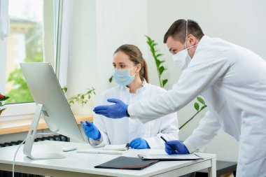 Tıbbi maskeli bir cerrah ve radyoloji uzmanı bilgisayarın ekranında bir hastanın röntgen fotoğraflarını tartışıyor. Masaüstü bilgisayarının önünde oturan bir kadın doktor, bir terapist yanında kalır..