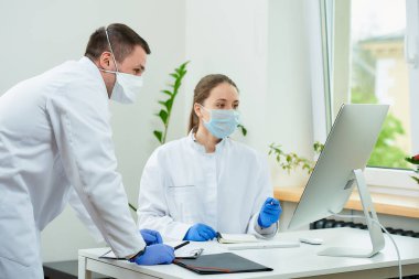 Tıbbi maskeli bir cerrah ve radyoloji uzmanı masaüstü bilgisayarında bir hastanın teşhisini tartışıyor. Bilgisayarın önünde oturan bir kadın doktor, yanında bir terapist oturuyor..