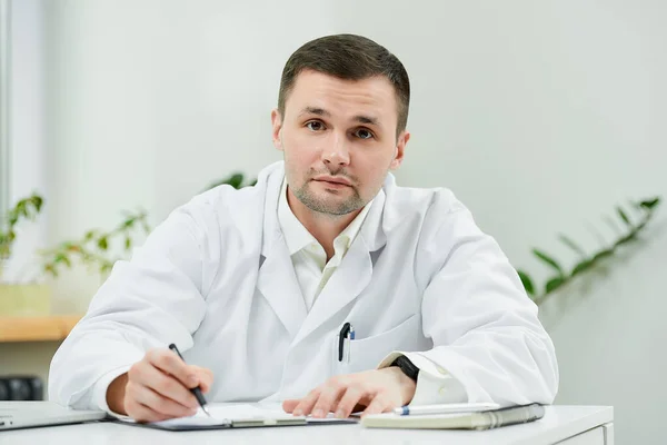 Médico Caucasiano Sério Jaleco Branco Está Sentado Sua Mesa Distraído — Fotografia de Stock
