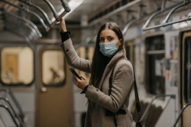 Coronavirus 'un yayılmasını önlemek için tıbbi maske takan bir kadın metro vagonuna bakıyor. Yüzünde COVID-19 maskesi olan bir kız trende cep telefonuyla poz veriyor..