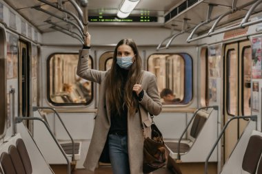 Koronavirüsün yayılmasını önlemek için maske takan bir kadın tırabzana tutunuyor ve metro vagonunun ortasında poz veriyor. COVID-19 'a karşı cerrahi maskeli bir kız bir metro treninde duruyor.