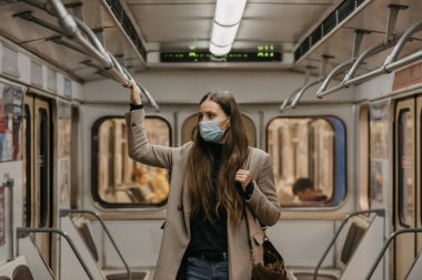 Coronavirus 'un yayılmasını önlemek için maskeli bir kadın metro vagonunun ortasındaki tırabzana tutunuyor. COVID-19 'a karşı cerrahi maskeli bir kız bir metro treninde duruyor..